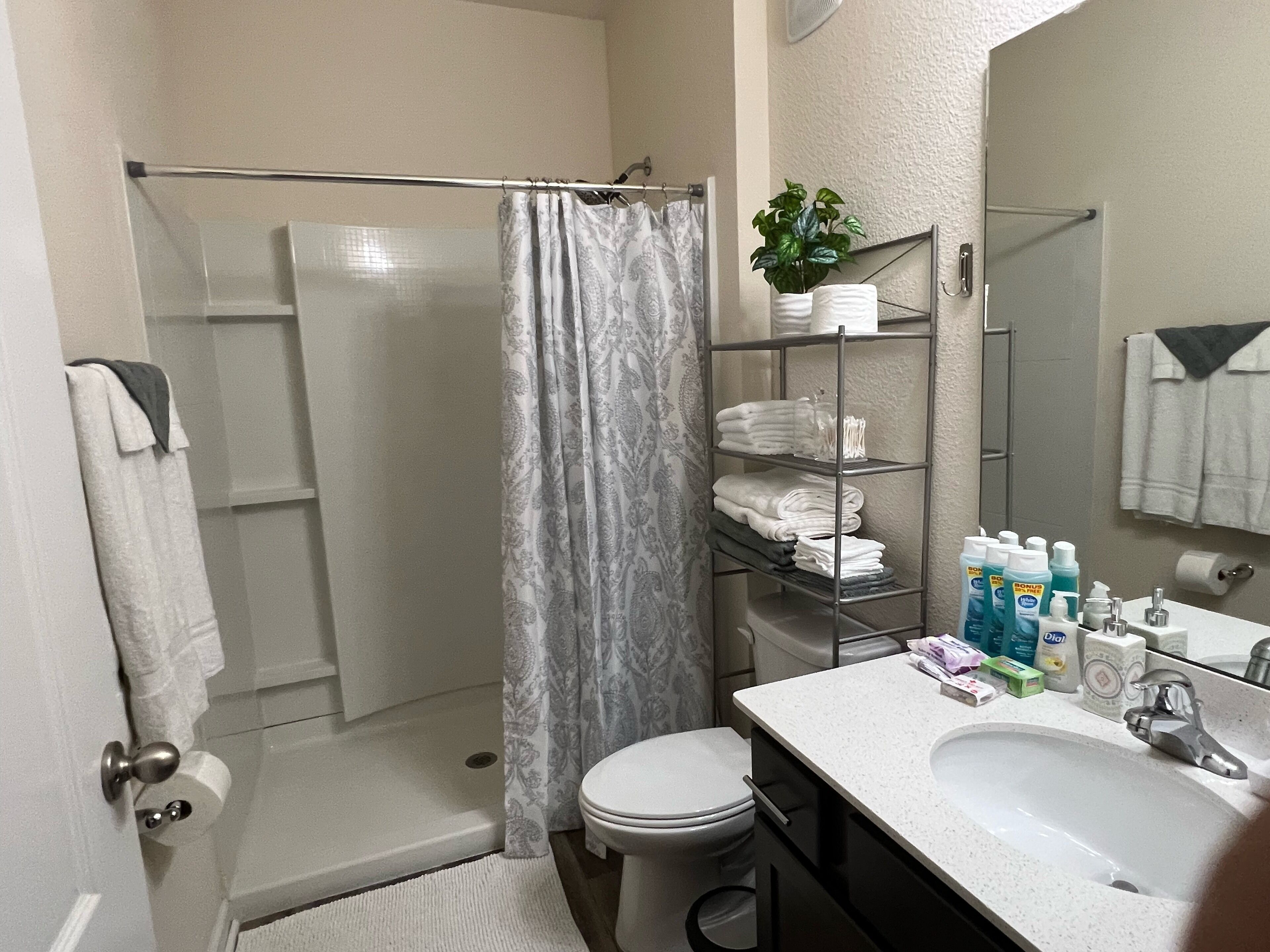 Een badkamer met douche, toilet, wastafel en een plank met toiletartikelen.
