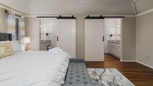 Een slaapkamer met een bed, een bankje, een plafondventilator en uitzicht op de badkamer.