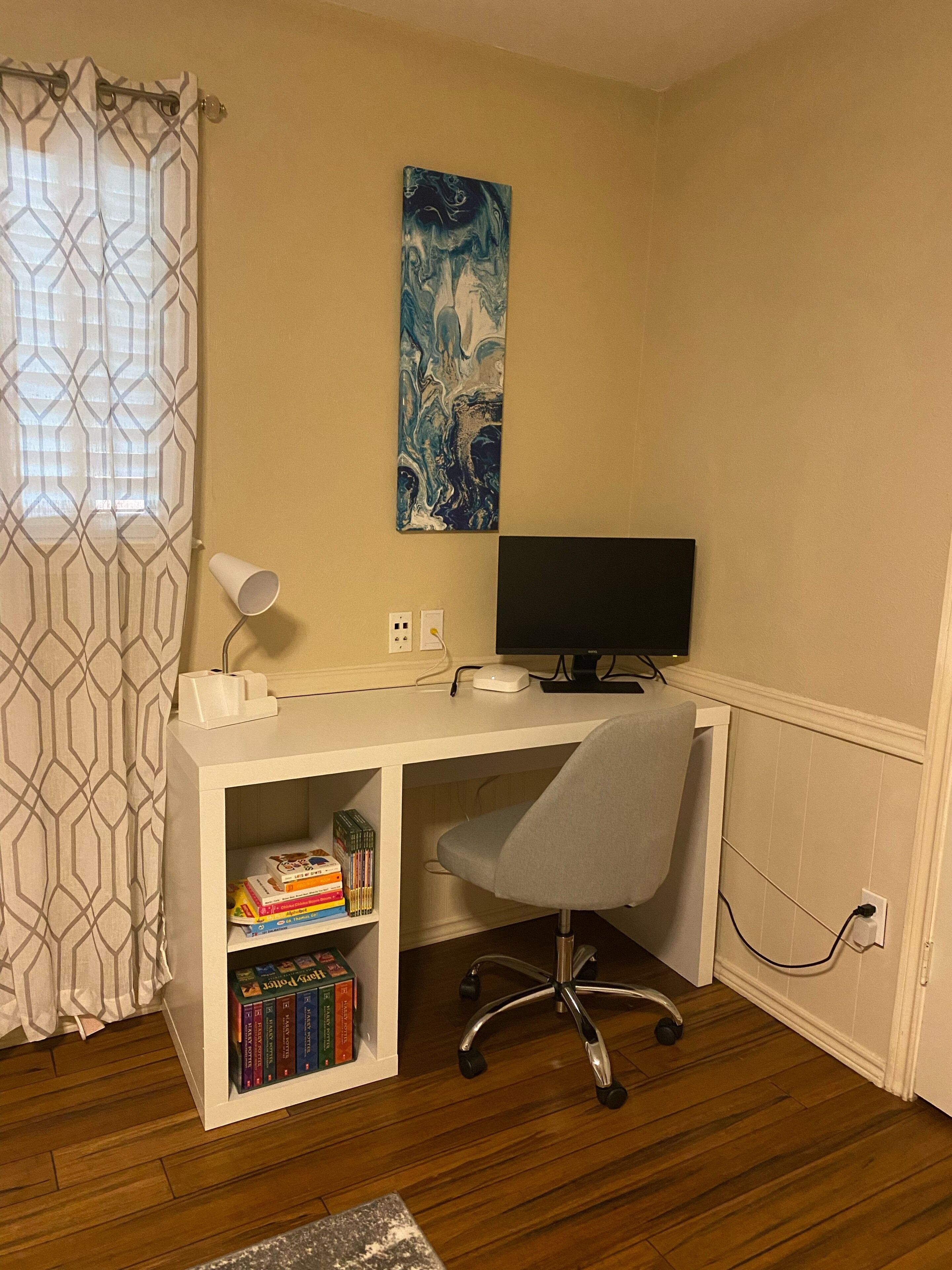 A study room with a desk, chair, bookshelf, and a painting on the wall.
