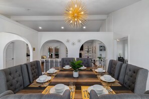 Comedor con una mesa de madera larga, sillas tapizadas de gris y una planta en el centro.