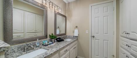 A bathroom with a granite countertop, two sinks, a large mirror, and a door.