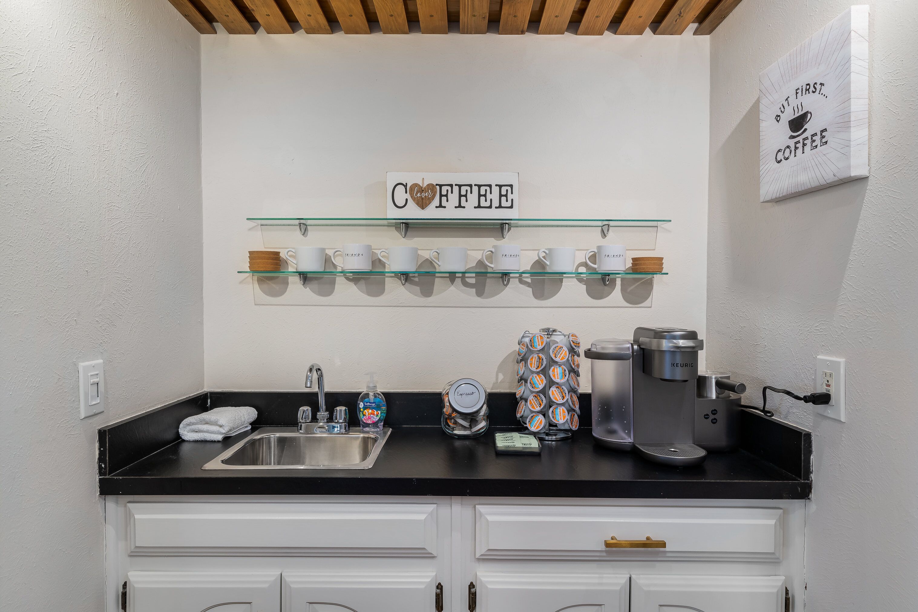 Eine Küche mit einer Kaffeestation, darunter eine Kaffeemaschine, Tassen und ein Schild mit der Aufschrift 'COFFEE'.