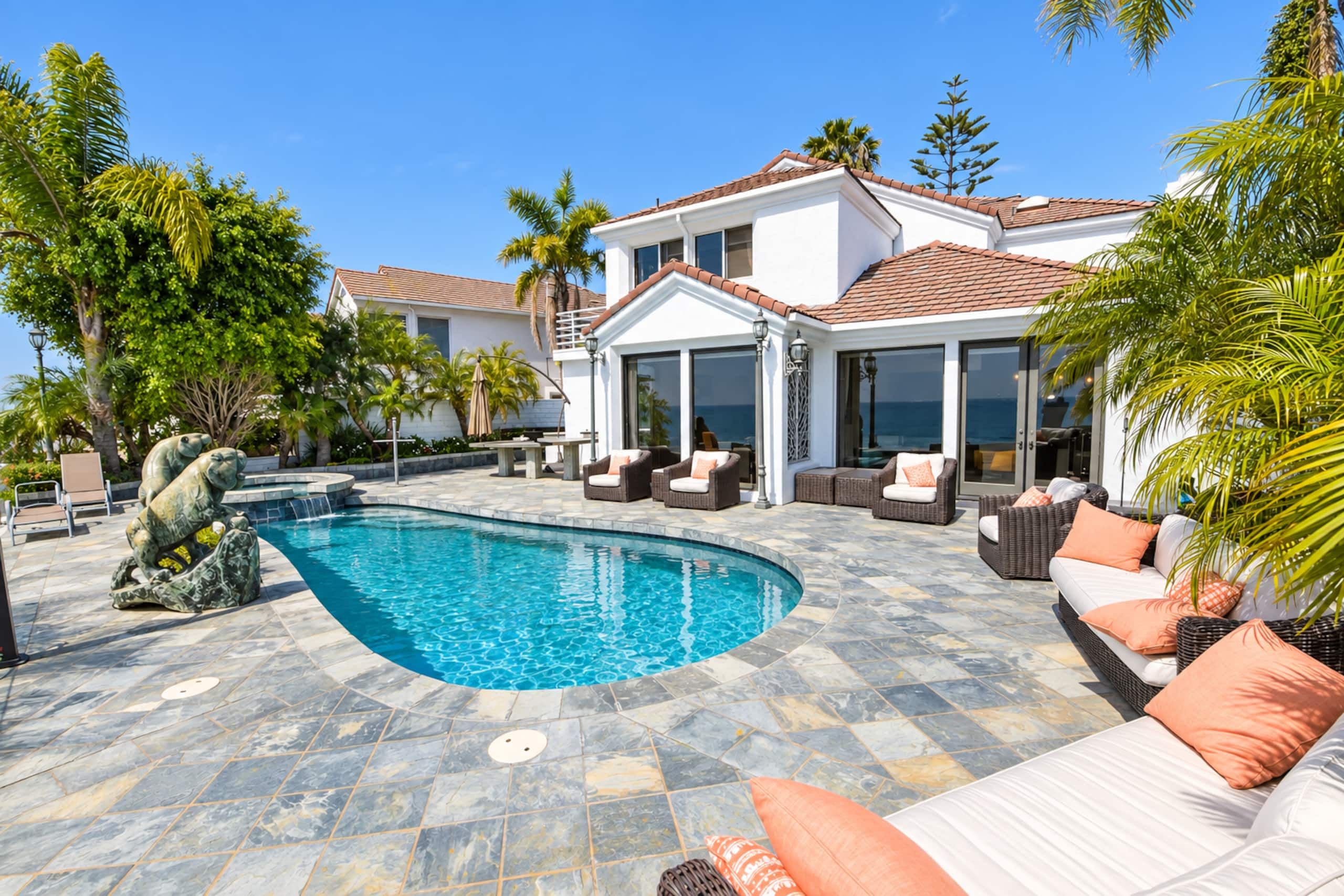 A pool area with a stone floor, outdoor furniture, and a statue.