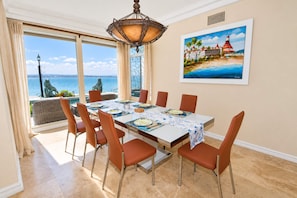 A dining area with a view of the sea, a painting of a coastal scene, and a chandelier.
