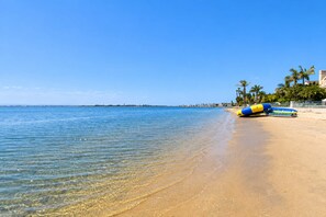 Ein Strand mit klarem Wasser, sandigem Ufer und einigen Palmen.