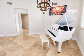 A spacious room with a white grand piano, a bench, and a chandelier. - Coronado Cays Beachfront with Private Pool & Spa (Coronado)