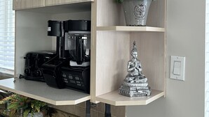 Una cocina con alacenas de madera clara, cafetera, planta en maceta y una estatua decorativa de Buda.