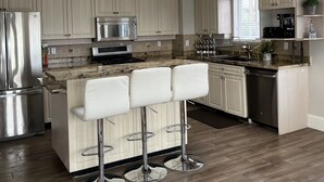 Una cocina moderna con una isla central, taburetes de bar, electrodomésticos de acero inoxidable y armarios de madera clara.
