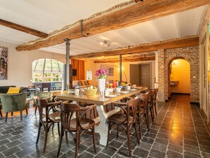 A spacious dining area with a long wooden table, multiple chairs, and a rustic brick wall. - Country house with garden for families (Merksplas)