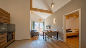Eine moderne Küche mit Holzausstattung und Einbauofen, ein Essbereich mit Tisch und Stühlen sowie ein Schlafzimmer mit Bett und Fenster.