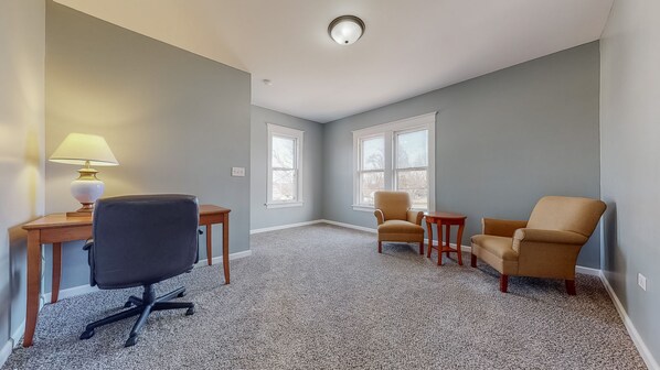 Een kamer met een bureau, twee fauteuils, een bijzettafeltje en een lamp.
