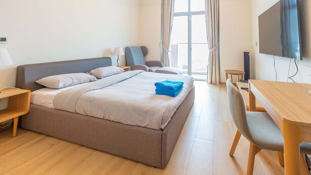 Habitación de hotel con una cama grande, un escritorio, una silla, un televisor y una ventana con cortinas.