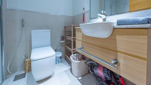 Un baño moderno con inodoro blanco, un lavabo con espejo y zona de ducha.
