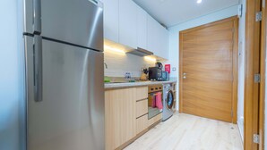 Una cocina compacta con un refrigerador de acero inoxidable, armarios de madera, un horno empotrado y una lavadora.
