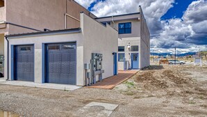 A modern building with two garage doors, a small attached structure, and a paved area with construction materials. - Salida Hideaway- New Studio Condo (Salida)