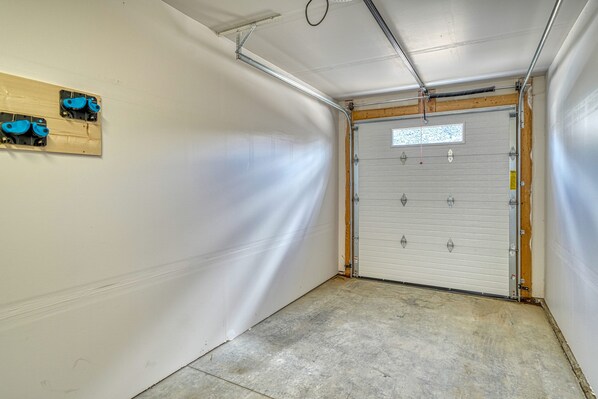 A garage with a white door, concrete floor, and a wooden shelf with blue objects.