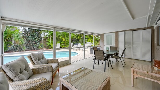 A modern indoor space with a glass wall overlooking a swimming pool, wicker furniture, and a dining area. - ‘Pelican Nest’, Tropical Naples Villa w/ Pool (Naples)