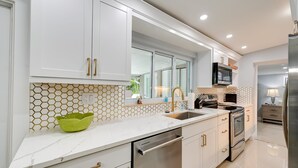 A modern kitchen with white cabinets, a stainless steel refrigerator, a microwave, and a dishwasher. - ‘Pelican Nest’, Tropical Naples Villa w/ Pool (Naples)