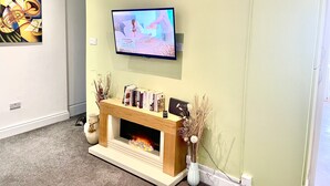 Un soggiorno con TV a schermo piatto montata a parete, un camino acceso e una libreria con libri e oggetti decorativi.
