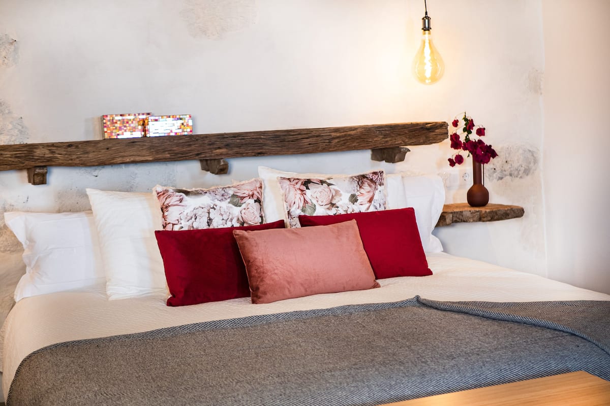 Un lit avec des oreillers blancs et rouges, une tête de lit en bois et un vase rempli de fleurs.