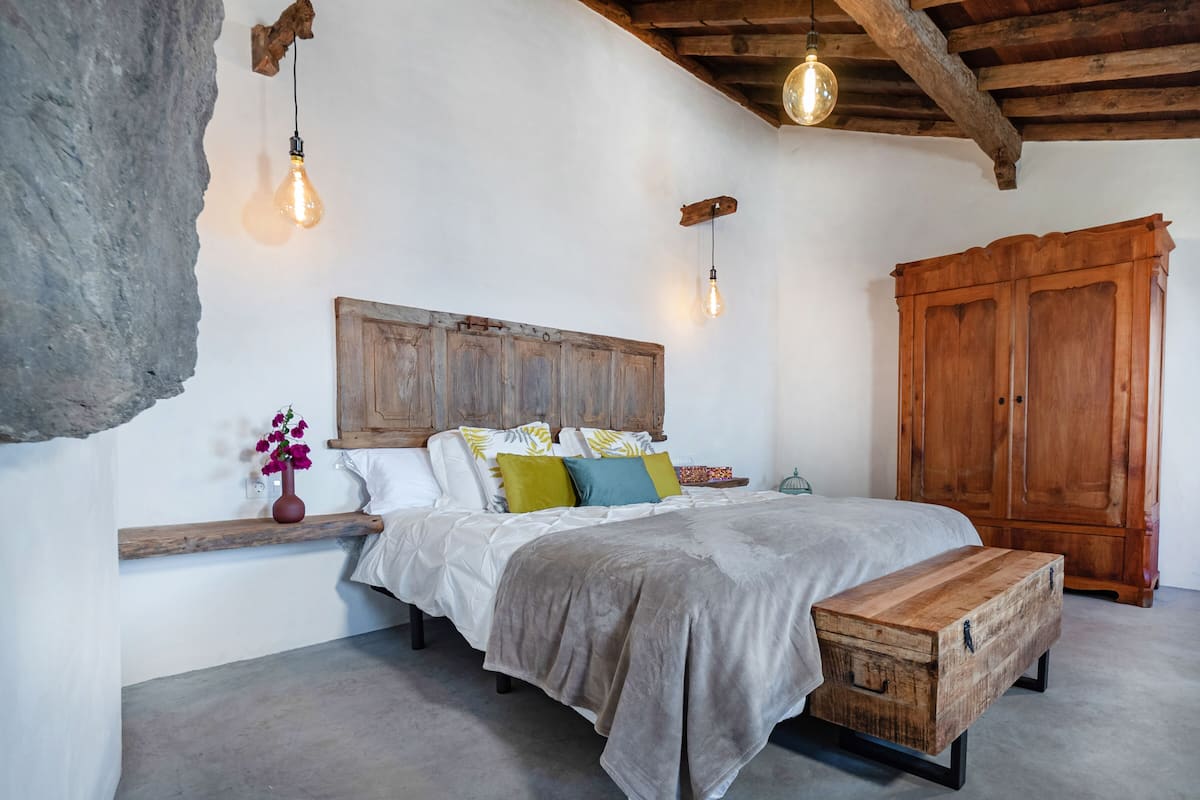 Une chambre à coucher avec une tête de lit en bois, un lit agrémenté de plusieurs oreillers, un banc en bois et une grande armoire en bois.