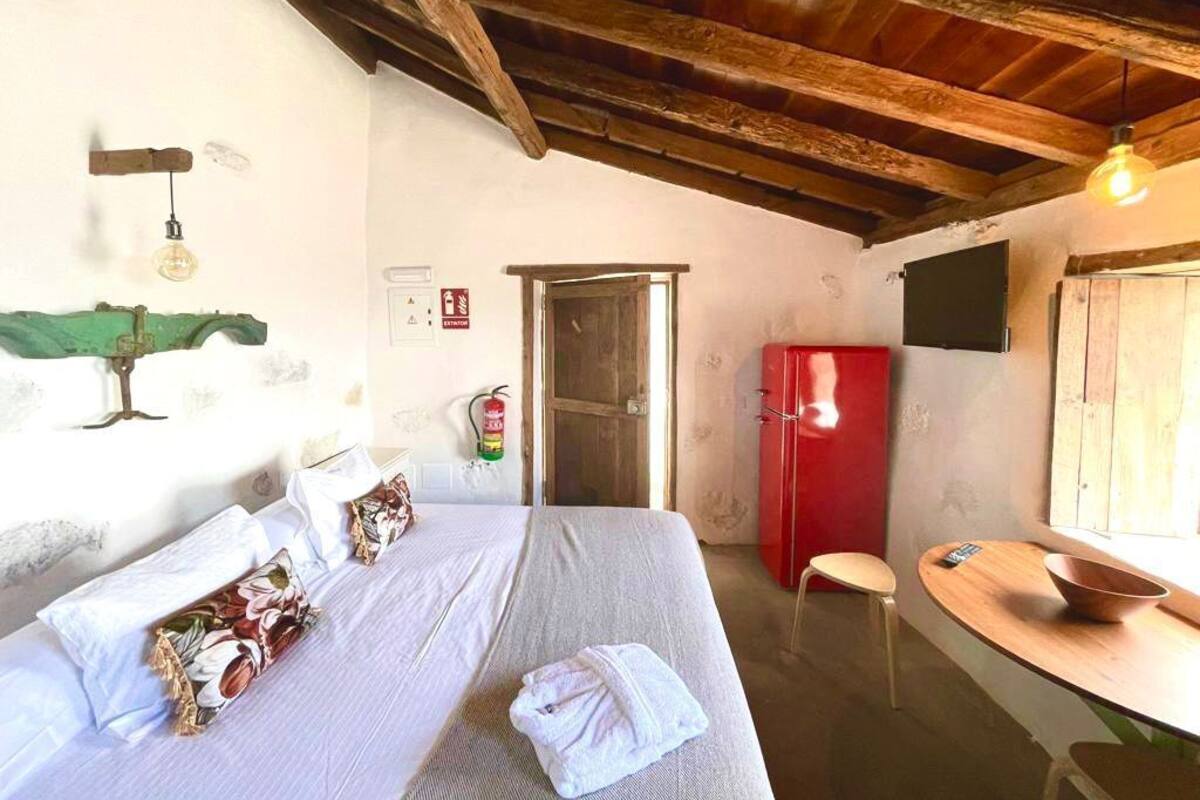 Une chambre à coucher avec un lit, un réfrigérateur rouge, une table en bois et une chaise.