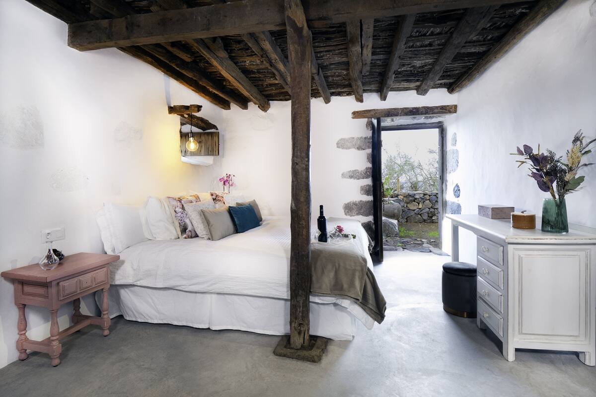 Une chambre à coucher avec un lit, une table de chevet, une commode et un mur en pierre.