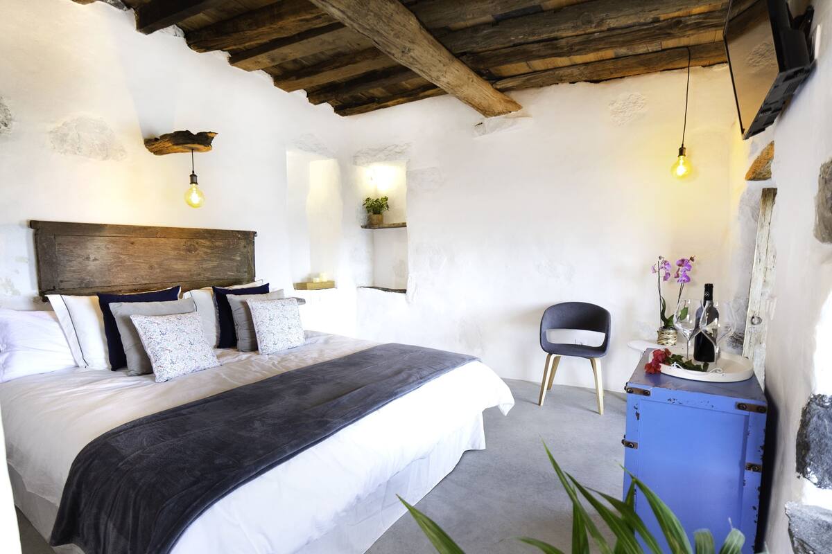 Une chambre à coucher avec une tête de lit en bois, un lit recouvert de draps blancs, une commode bleue et une chaise.