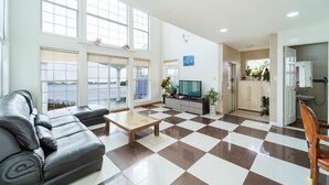 A spacious living room with a checkered floor, a leather sofa, a wooden coffee table, and a television. - Daebudo Fullhouse Pension (Ansan)