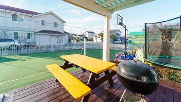 A covered outdoor area with a barbecue grill, picnic table, and sports field.