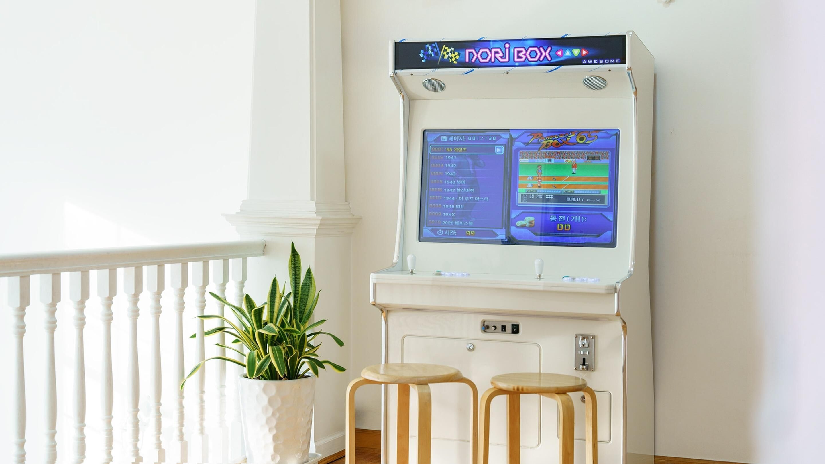 A Pachinko machine with a digital display, two stools, and a potted plant.