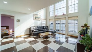 A spacious living room with a checkered floor, a leather sofa, and large windows offering a view of the water. - Daebudo Fullhouse Pension (Ansan)