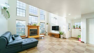 A spacious living room with a fireplace, a large window, a flat-screen TV, and a sofa.