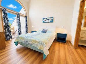 A bedroom with a bed, nightstands, a lamp, a painting, and a view through a window.