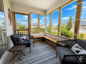 A sunroom with large windows, a wooden bench, and two wicker chairs.