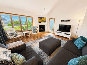 A living room with a fireplace, a television, and a large window overlooking a green landscape.