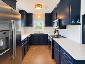 A modern kitchen with dark cabinetry, stainless steel appliances, and a white countertop.