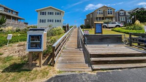 A wooden boardwalk leading to a beach area with a small kiosk and a signboard. - The Last Resort ⛱️High on a dune with spectacular views - 4 BR/2 BA oceanside home in Duck⛱️ (Duck)