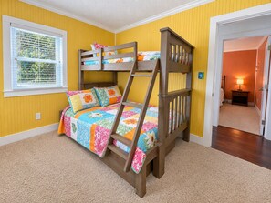 A bunk bed in a room with yellow walls, a window with blinds, and a carpeted floor.
