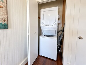 A laundry room with a stacked washer and dryer, wooden flooring, and a door with a white panel.
