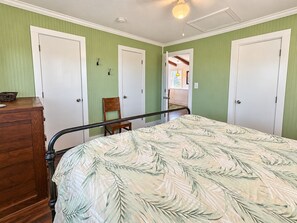 A bedroom with a bed, a wooden dresser, and a chair. There are two white doors and a window.