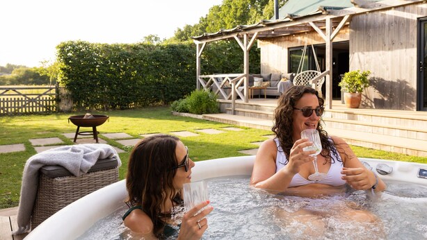 Zwei Personen in einer Außenwhirlpoolanlage mit einer Holzterrasse und einer überdachten Terrasse im Hintergrund.