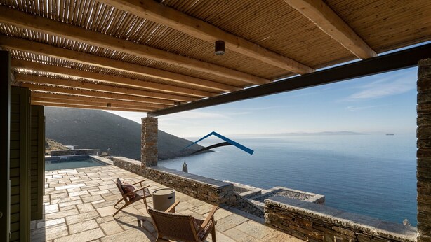 Une terrasse extérieure dotée d’un sol en pierre, de poutres en bois et offrant une vue sur la mer.