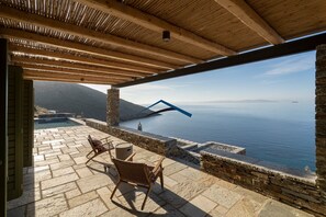 An outdoor terrace with stone flooring, wooden beams, and a view of the sea.
