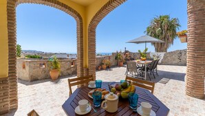 Une terrasse avec une table dressée pour deux, entourée de murs en pierre et de plantes en pot, offrant une vue panoramique.