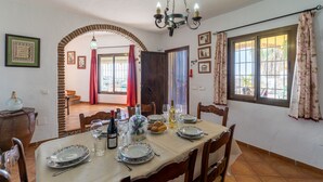 Un coin repas avec une table dressée pour quatre personnes, un lustre et une vue sur l’extérieur à travers une fenêtre ornée de rideaux.