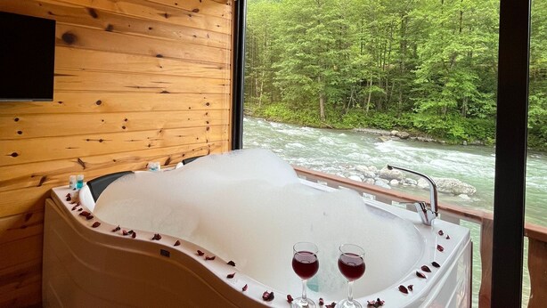 A wooden cabin interior with a large bathtub filled with bubbles, two glasses of red wine, and a red exercise ball. - Teona Caglayan Bungalov (Findikli)