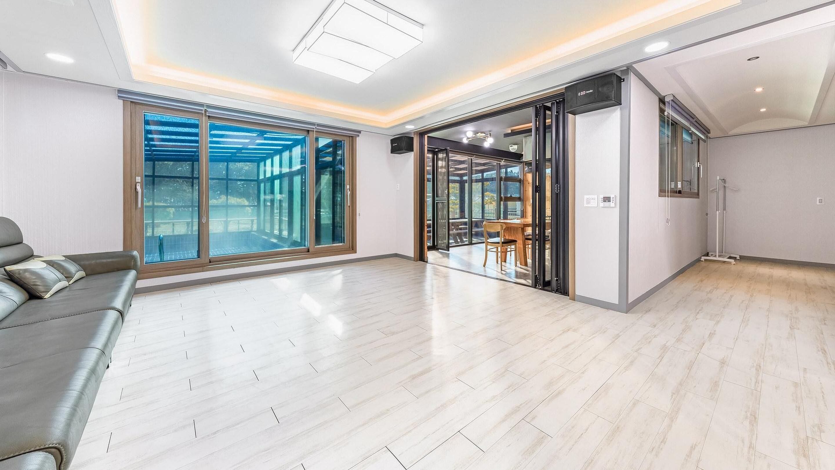 A spacious living area with a grey sofa, large sliding glass doors leading to a balcony, and a dining area with a table and chairs.