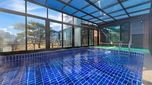 An indoor swimming pool with blue tiles, large windows, and a view of the outside. - Daebudo Juni Pension (Ansan)