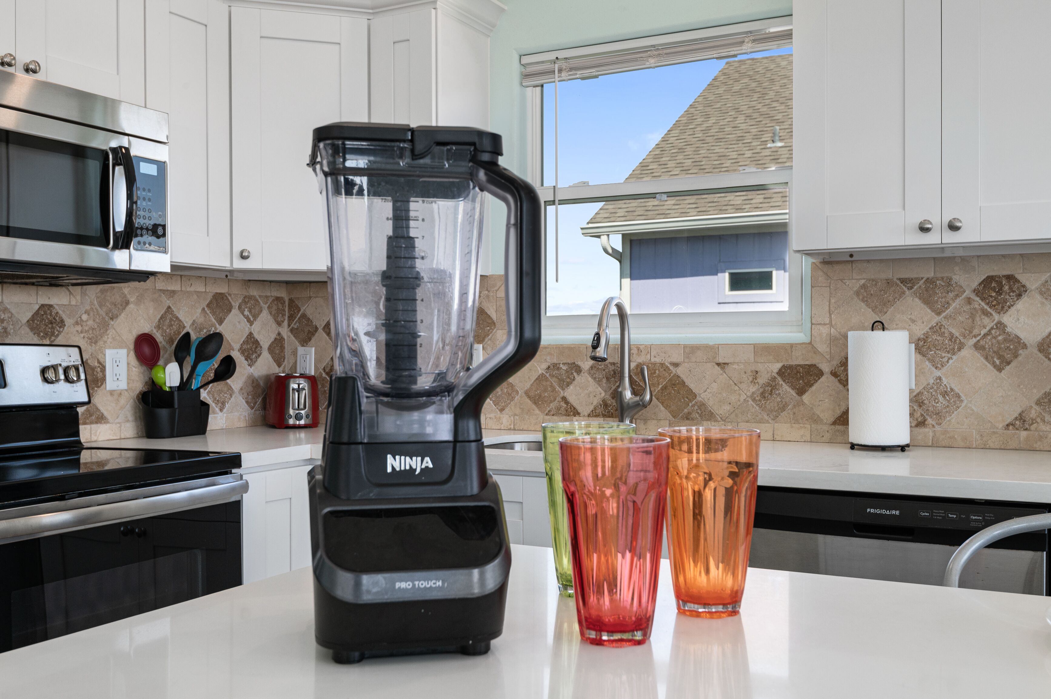 A kitchen with a Ninja Pro Touch blender, a toaster, and a window with a view of a house.